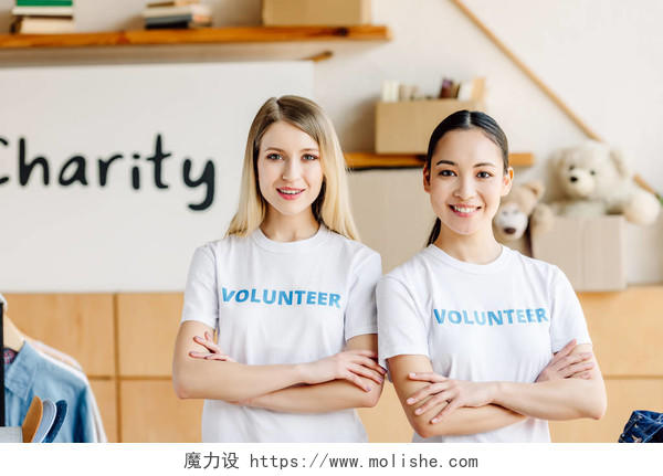 两个美丽的多元文化志愿者女孩交叉手臂微笑，看着相机